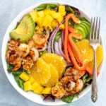 Pinterest Pin with text overlay 'Shrimp & Avocado Salad with Orange Vinaigrette'. Image of large bowl filled with mixed greens, grilled shrimp, avocado, and oranges.