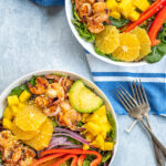 Pinterest Pin with text overlay 'Orange Shrimp Salad with Avocado & Mango'. Image of two large bowls filled with mixed greens, grilled shrimp, avocado, and oranges.