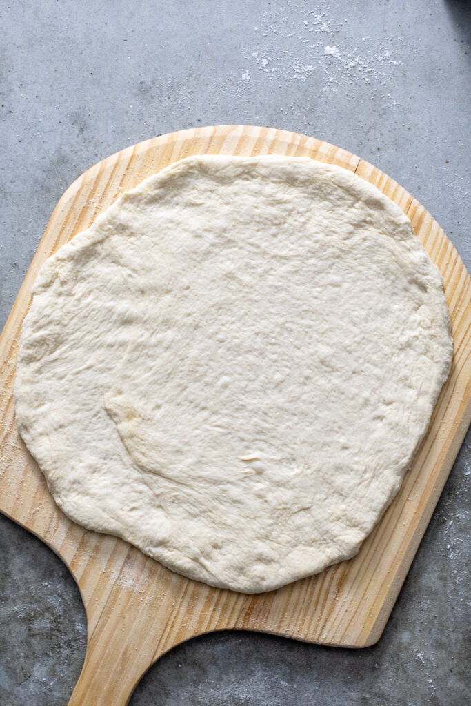 Homemade Pizza Dough stretched out and laid down on a wooden pizza peel.