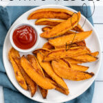 Pinterest Pin with text 'Baked Sweet Potato Wedges'. Image of plate with crispy sweet potato wedges and a little cup of ketchup