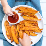 Pinterest Pin with text 'Baked Sweet Potato Wedges'. Image of plate with crispy sweet potato wedges and a little cup of ketchup