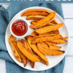 Pinterest Pin with text 'Baked Sweet Potato Wedges'. Image of plate with crispy sweet potato wedges and a little cup of ketchup