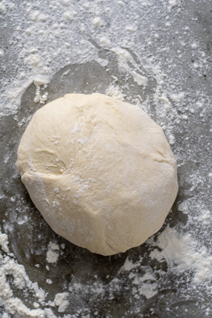 A ball of flour covered dough sitting on a counter top.