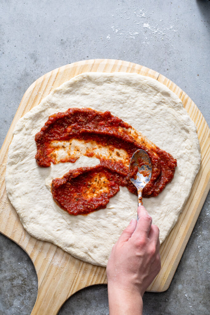 Sauce being smeared onto fresh homemade pizza dough.