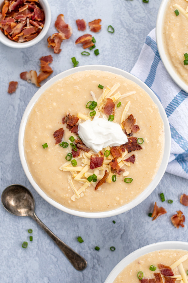 Overhead view of a large white bowl filled with baked potato soup topped with smoked gouda cheese, bacon crumbles, green onions, and sour cream.
