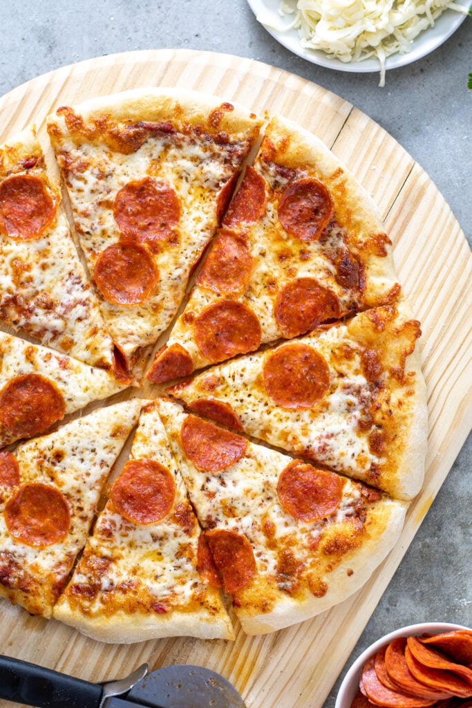 Close up of a freshly cooked and cut pizza on a wooden pizza peel showing of melted cheese and cooked pepperoni.