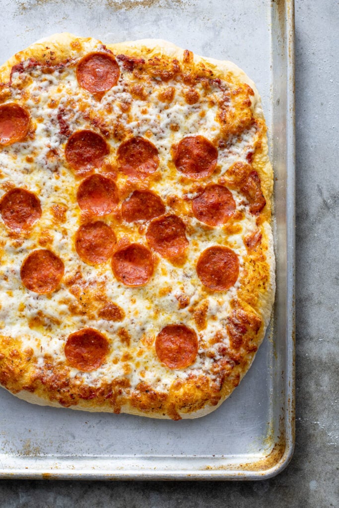 Cooked pizza with melted cheese and pepperoni on a sheet pan.