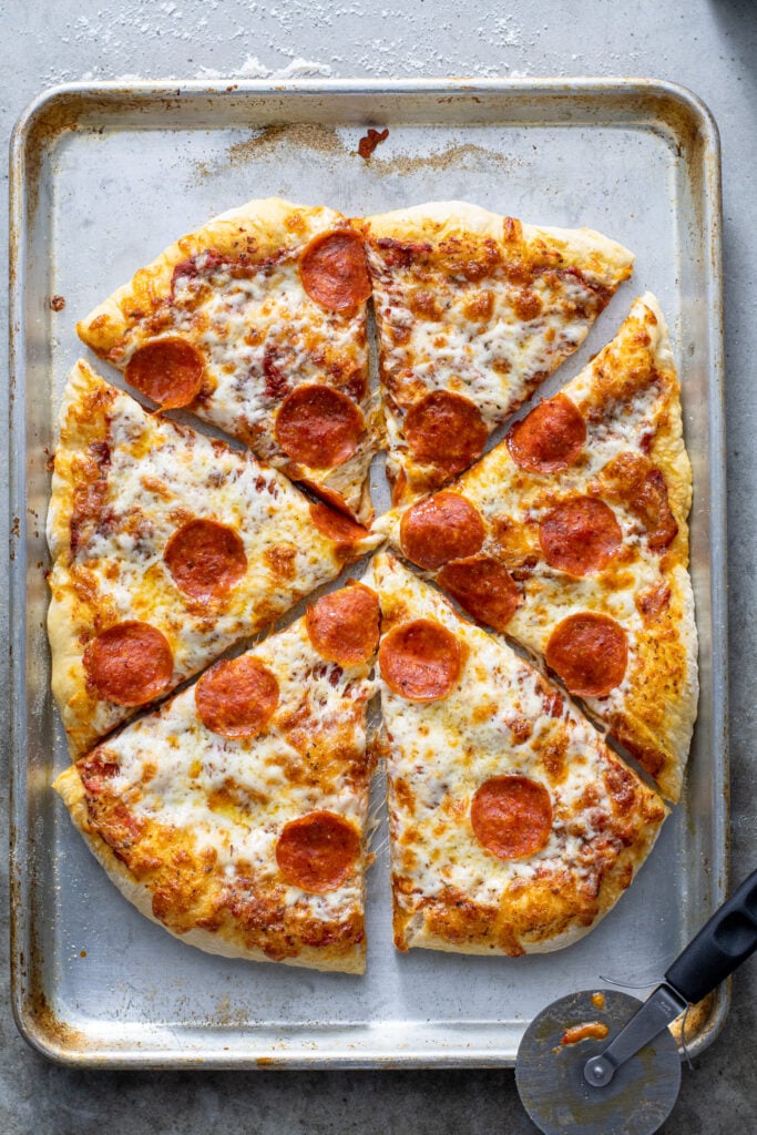Cut pizza on a sheet pan with a pizza cutter laying next to it.