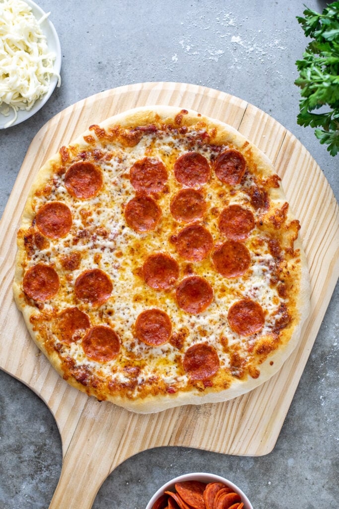 Freshly pulled out of the oven a pepperoni pizza sits on a wooden pizza peel waiting to be cut.