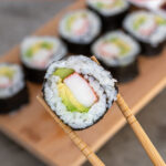 Pinterest Pin with text overlay 'California Sushi Rolls', image of sushi roll being held by chopsticks.