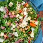 Pinterest Pin with text over lay 'Easy to Make Antipasto Salad', image of a bowl of arugula topped with the ingredients of the salad.