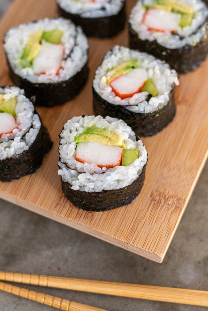 Platter of California rolls focused in on a roll in front showing off crab, cucumber, and avocado.