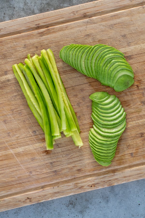 Sliced cucumber and avocado on a cutting board.