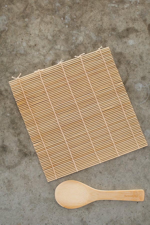 Bamboo sushi mat and a bambo rice paddle sitting on a countertop.