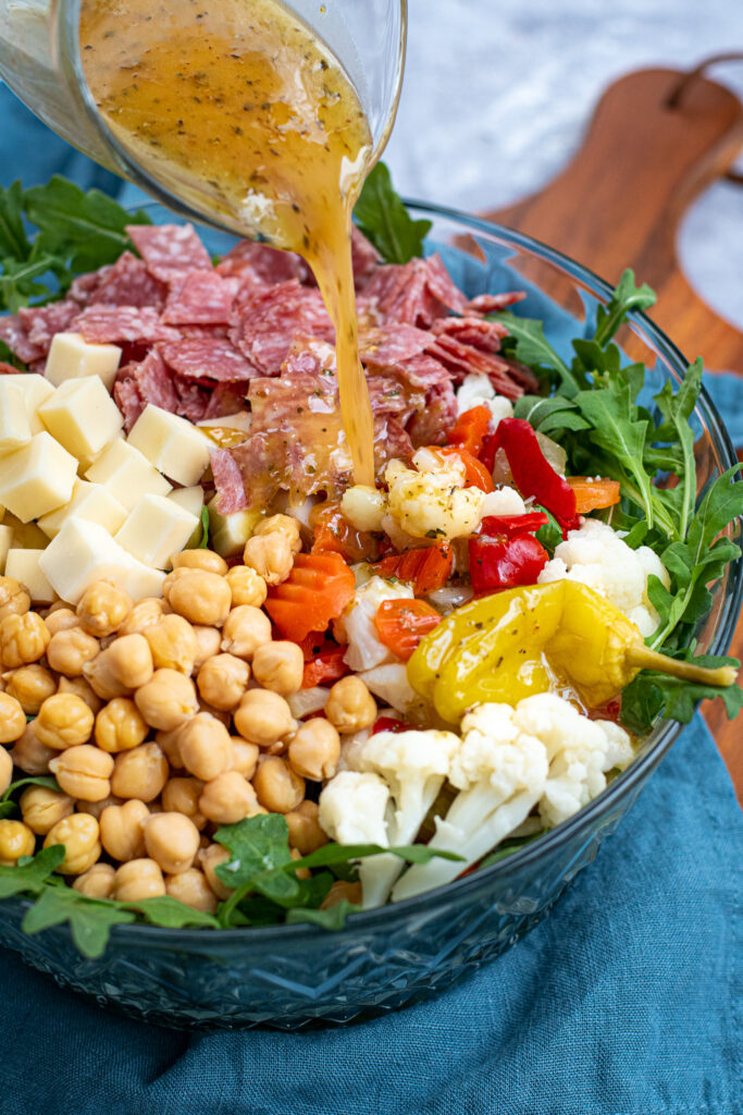 Homemade oregano dressing being poured over a bowl of antipasto salad.