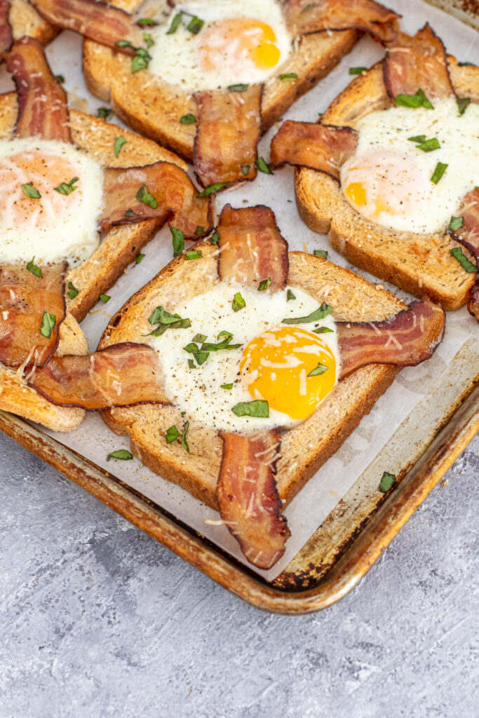 Angled close up shot of a toasted egg in a hole with bacon on a sheet pan.