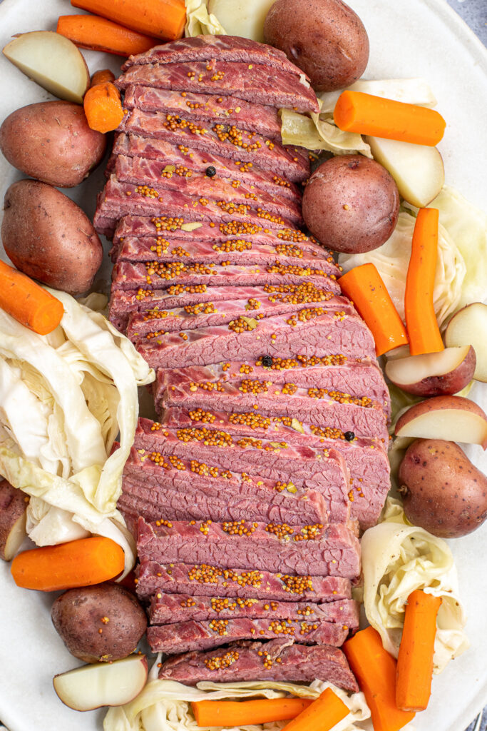 Freshly cooked and cut corned beef laid out on a cream platter with cabbage and carrots.