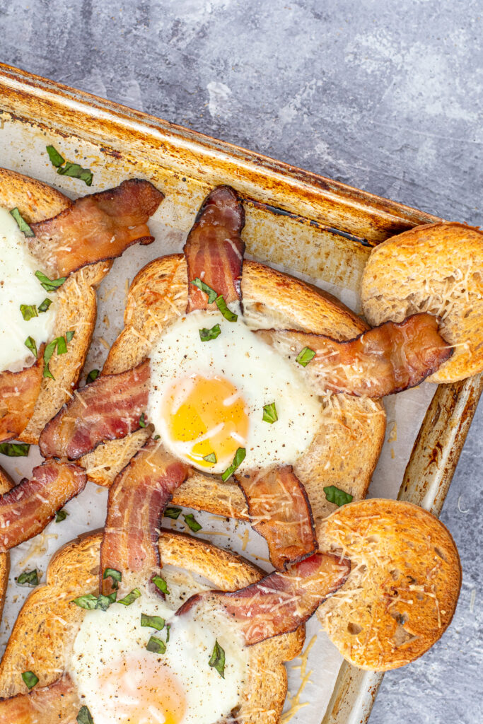 Close up of an egg in the hole with bacon strips showning a yellow yolk and crispy parmesan cheese.