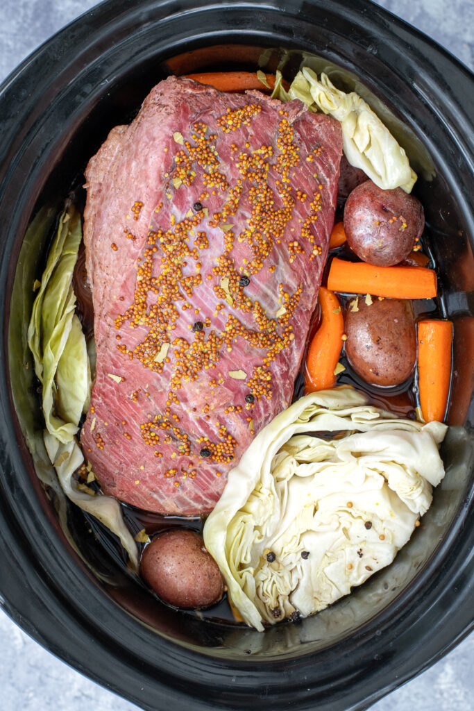 Overhead of a Crockpot filled with a cooked corned beef, cabbage, potatoes, and carrots.