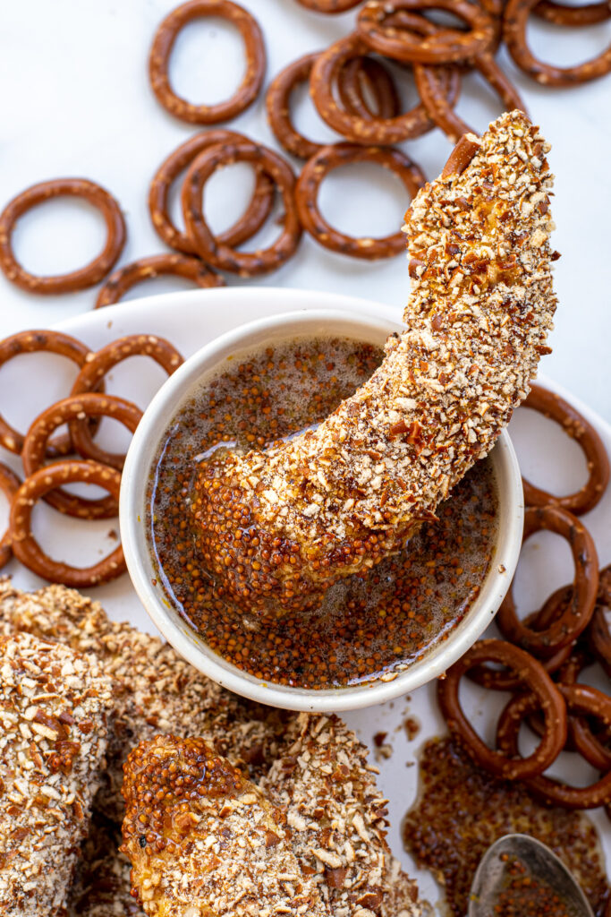 Pretzel Crusted Chicken Tender dipped in and resting in a small bowl of honey mustard sauce.