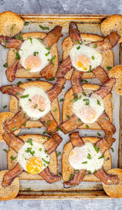 A sheet pan full of freshly baked egg in a hole with bacon garnished with sprinkled greens.