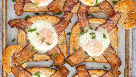 A sheet pan full of freshly baked egg in a hole with bacon garnished with sprinkled greens.