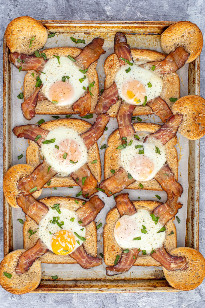 A sheet pan full of freshly baked egg in a hole with bacon garnished with sprinkled greens.