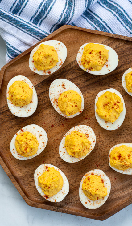 Wooden platter filled with many easy deviled eggs, garnished with sprinkles of red paprika.