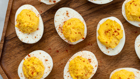 Wooden platter filled with many easy deviled eggs, garnished with sprinkles of red paprika.