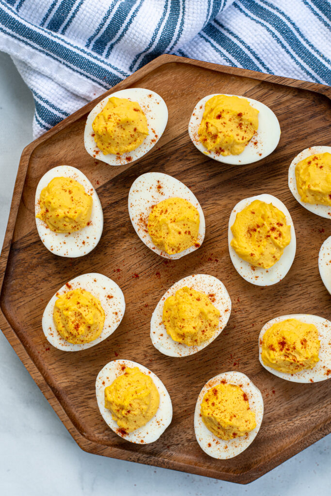 Wooden platter filled with many easy deviled eggs, garnished with sprinkles of red paprika.