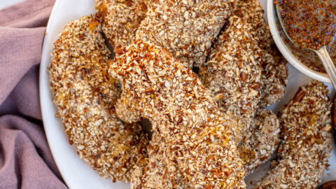 Plate full of a stack of Pretzel Crusted Chicken Tenders next to a small bowl of honey mustard.
