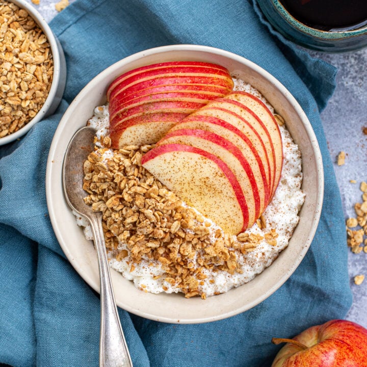 Overhead view of a breakfast table with a bowl full of cottage cheese and apple with granola and cinnamon.