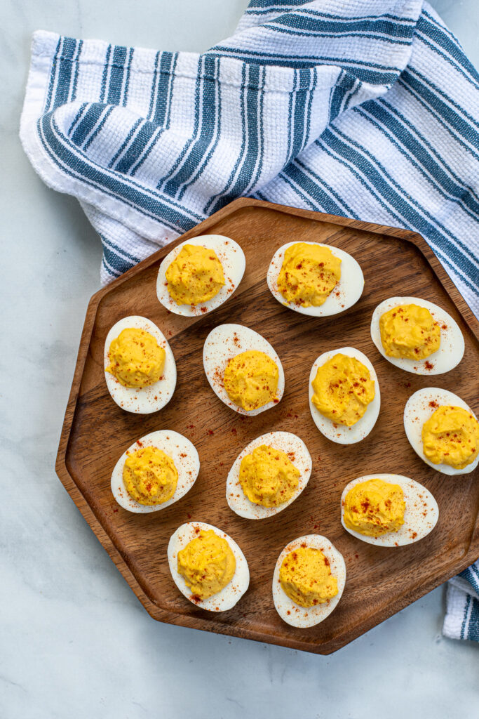 Flatly of an octagonal shaped wood cutting board filled with easy deviled eggs next to a blue and white striped towel.