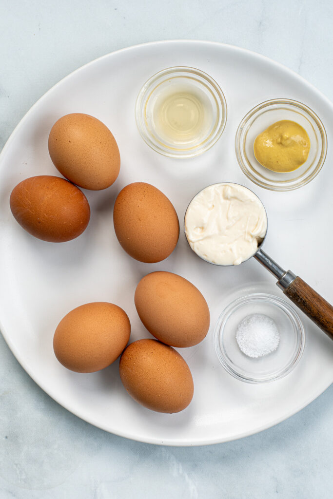 Ingredients to make deviled eggs laid out on a white plate.