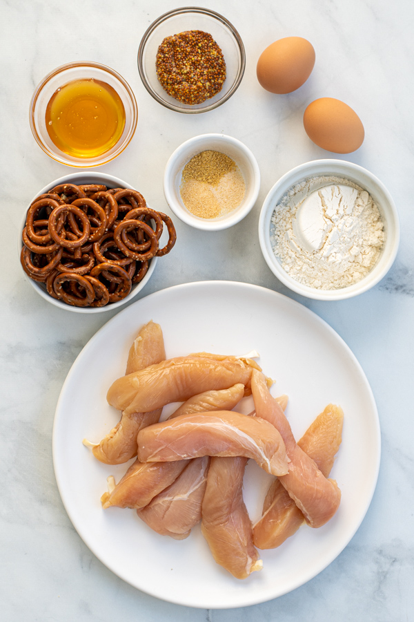 Ingredients for pretzel crusted chicken tenders sitting on a table top.