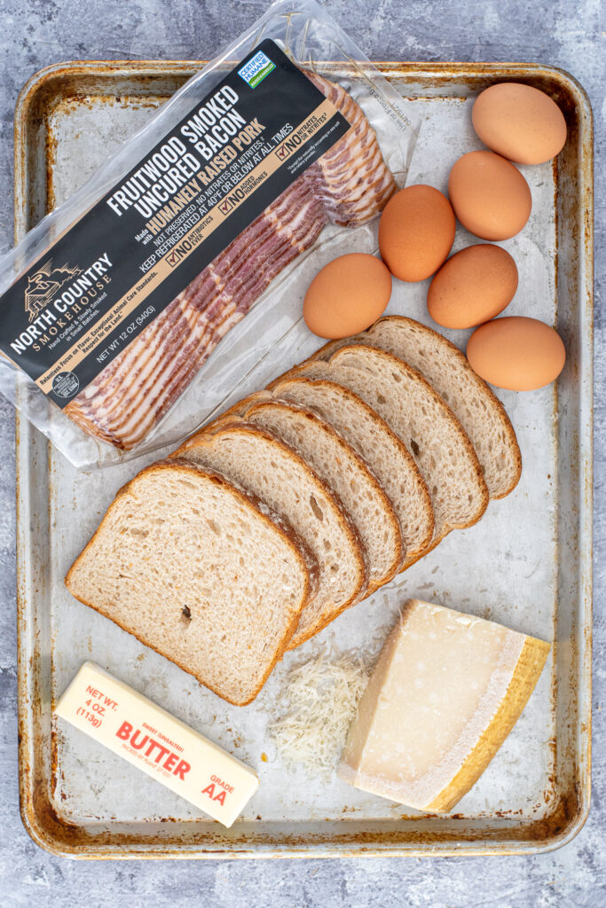 All the ingredients needed for baked egg in a hole laid out on a sheet pan.