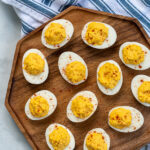 Pinterest Pin with text 'Simple & Easy Deviled Eggs', image of many deviled eggs laid out on a wood plater garnished with red paprika.