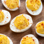 Pinterest Pin with text 'Simple & Easy Deviled Eggs', image of many deviled eggs laid out on a wood plater garnished with red paprika.