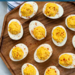Pinterest Pin with text 'Simple & Easy Deviled Eggs', image of many deviled eggs laid out on a wood plater garnished with red paprika.