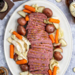 Pinterest Pin with text 'Slow Cooker Guinness Corned Beef and Cabbage', Image of platter with slices of corned beef and vegetables.