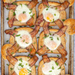 Pinterest Pin with text overlay 'Sheet Pan Egg in a Hole', image of a sheet pan with six baked egg in a hole toasts' with bacon.
