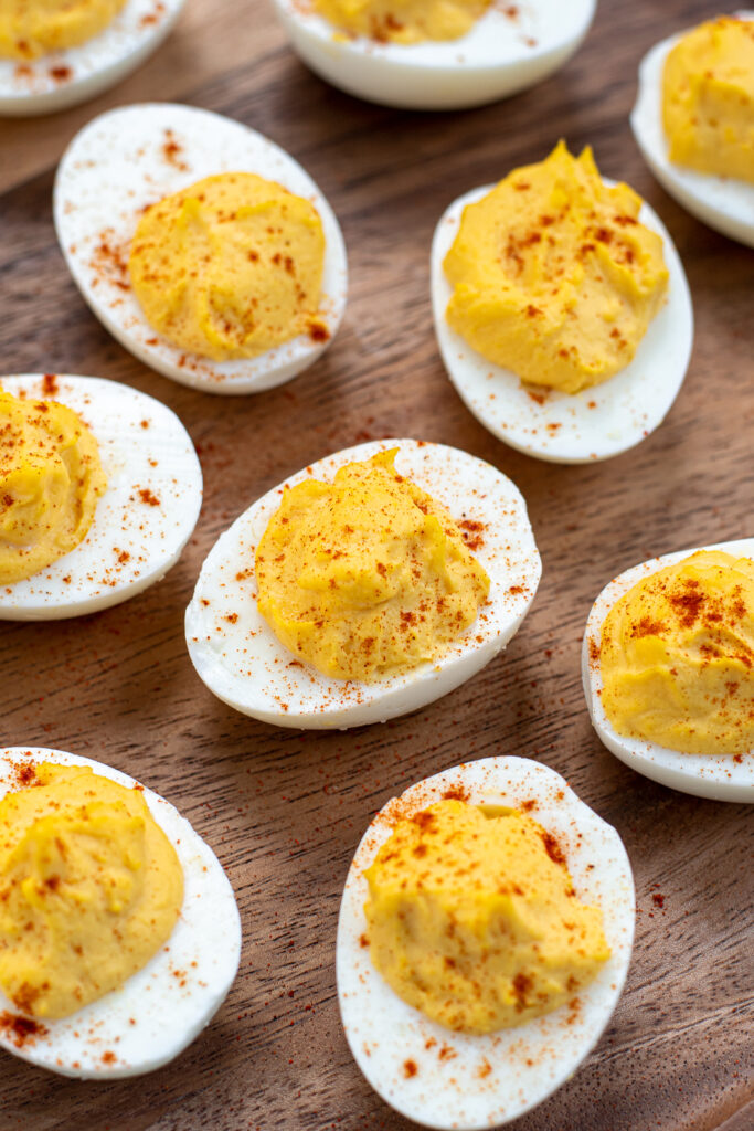 Focus on a deviled egg in the center of a wooden platter full of deviled eggs garnished with paprika.