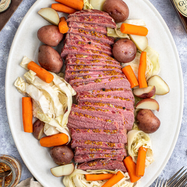 Sliced Corned Beef and a large platter next to sliced cabbage, carrots, and potatoes.