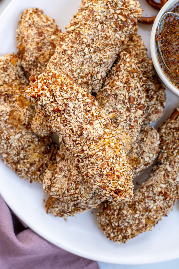 A stack of pretzel crusted chicken tenders on a plate.