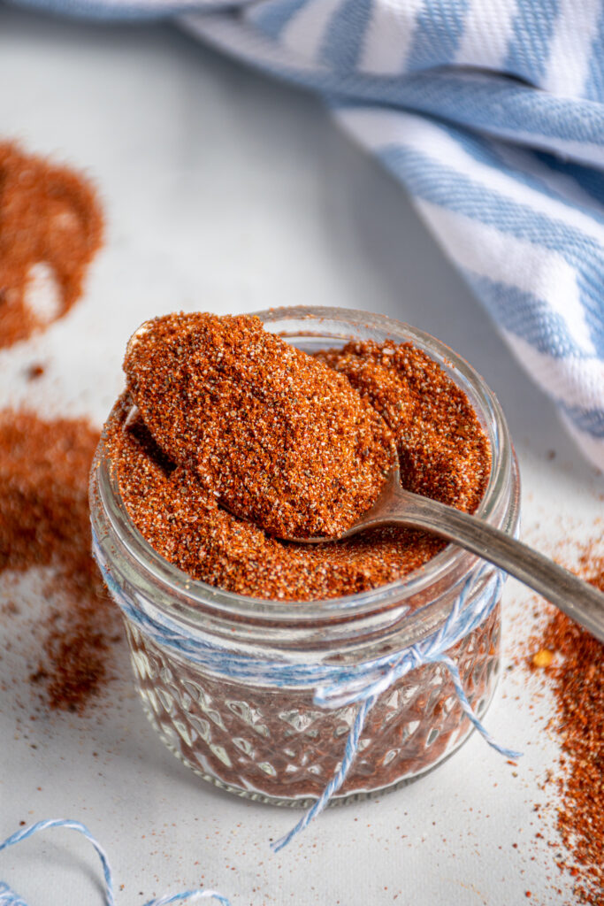 Close up of a spoon full of fajita seasoning resting on a jar full of spices.