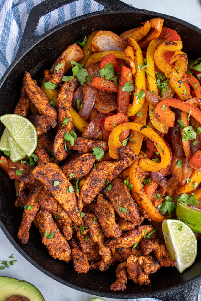 Close up of chicken fajitas in a cast iron next to colorful bell peppers.