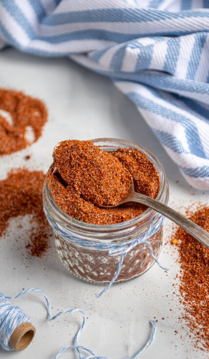 Spoon filled with fajita seasoning laying on top of a full jar of spices.