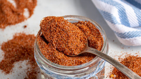 Spoon filled with fajita seasoning laying on top of a full jar of spices.