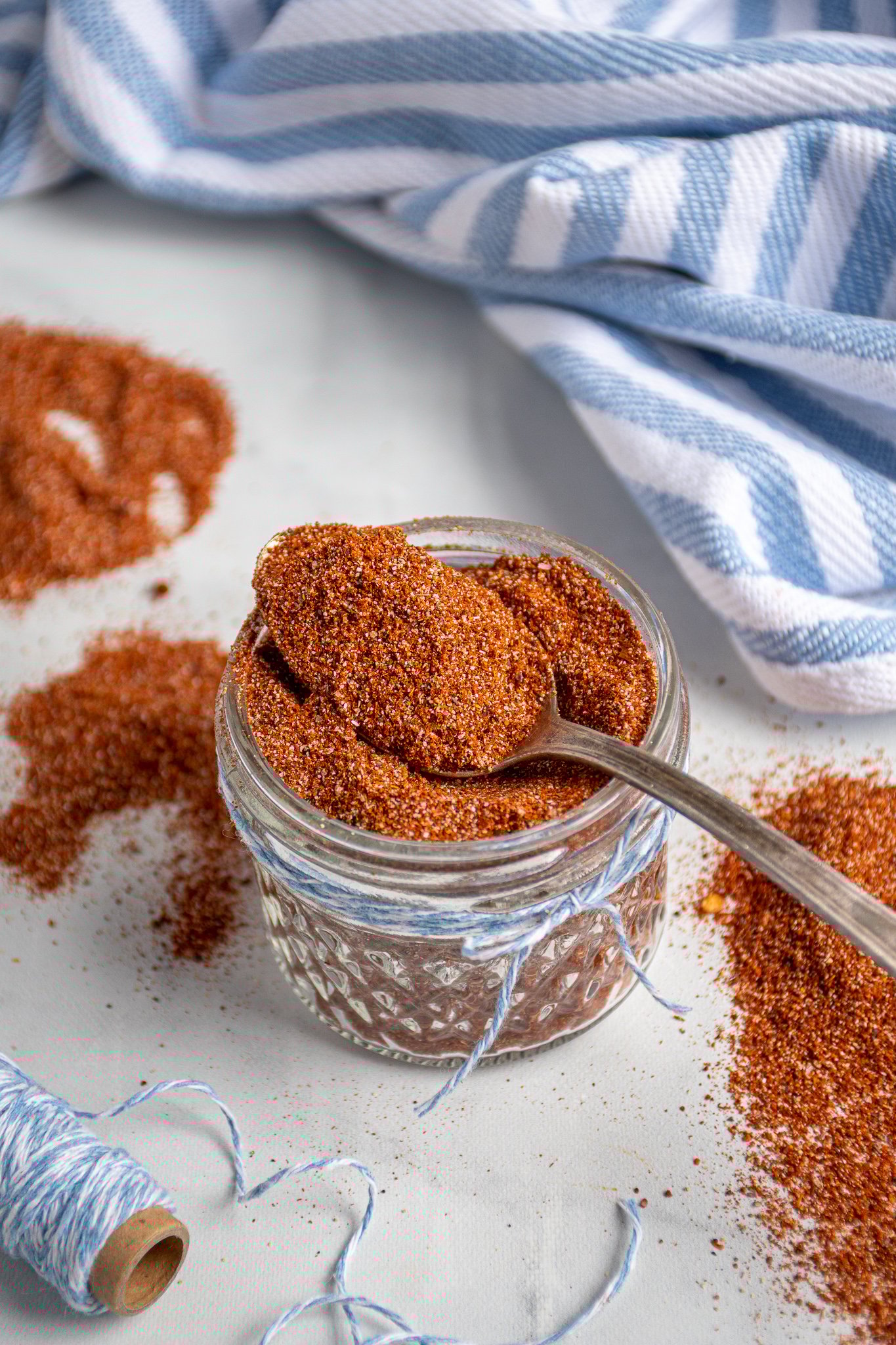 Spoon filled with fajita seasoning laying on top of a full jar of spices.