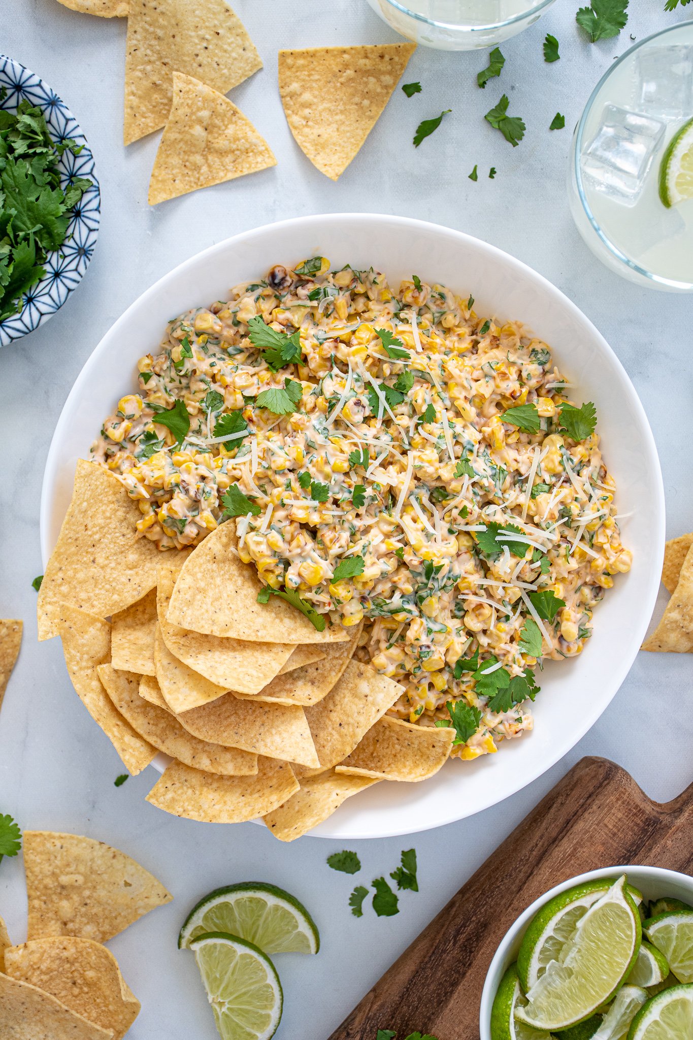 Large what bowl filled with Mexican Street Corn Dip and tortilla chips surrounded by more chips, cilantro, and limes.